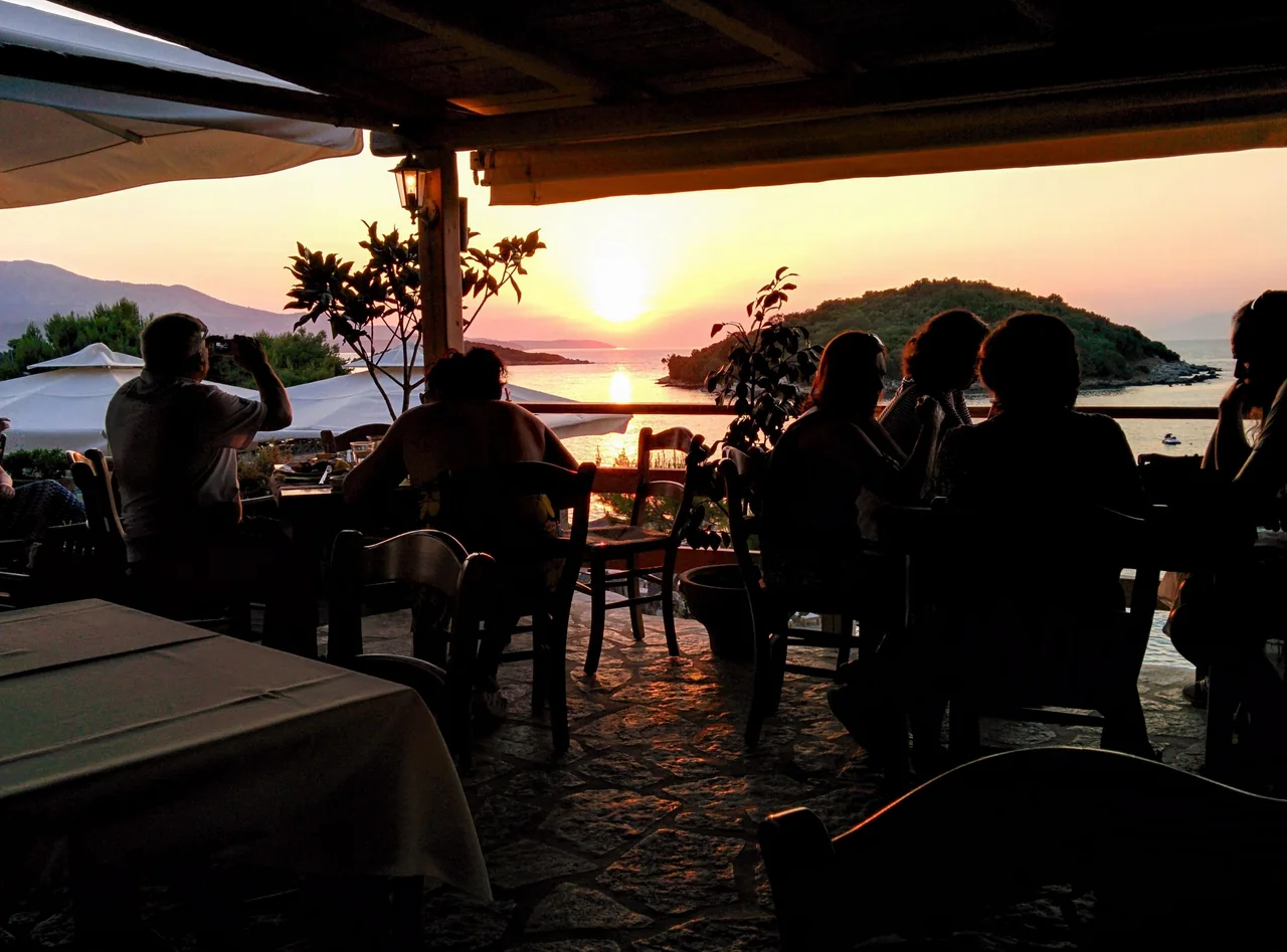 Njerëz që kalojnë mbrëmjen së bashku në një restorant buzë detit në Ksamil, ndërsa dielli perëndon mbi ujë