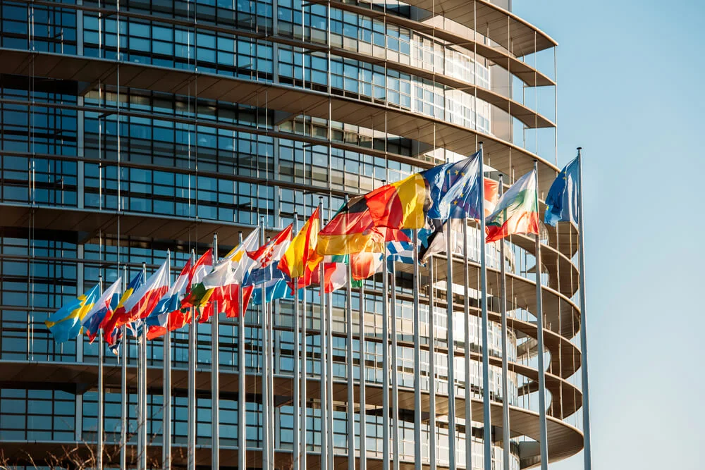 Flamuj evropianë përpara një ndërtese moderne institucionale me fasadë xhami