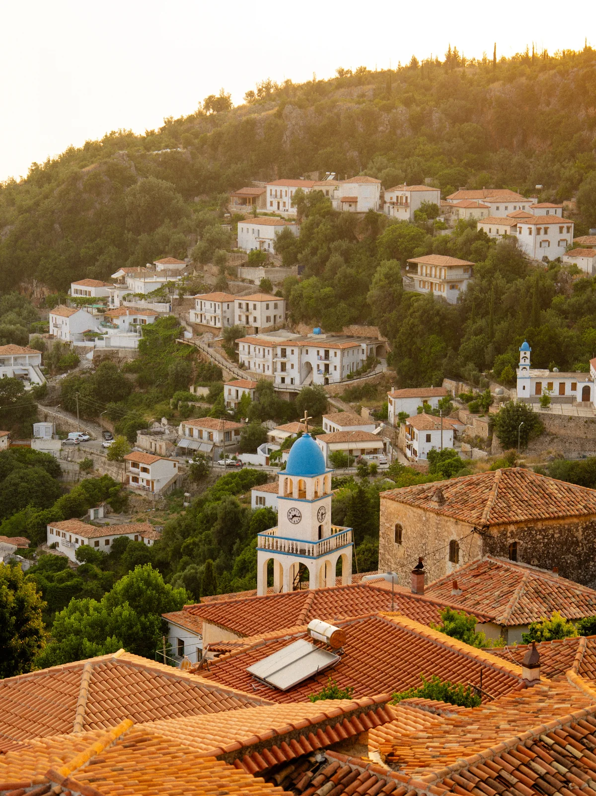 Fshat mesdhetar në kodër me çati prej terrakote dhe kambanore me kupola blu në dritën e artë të diellit
